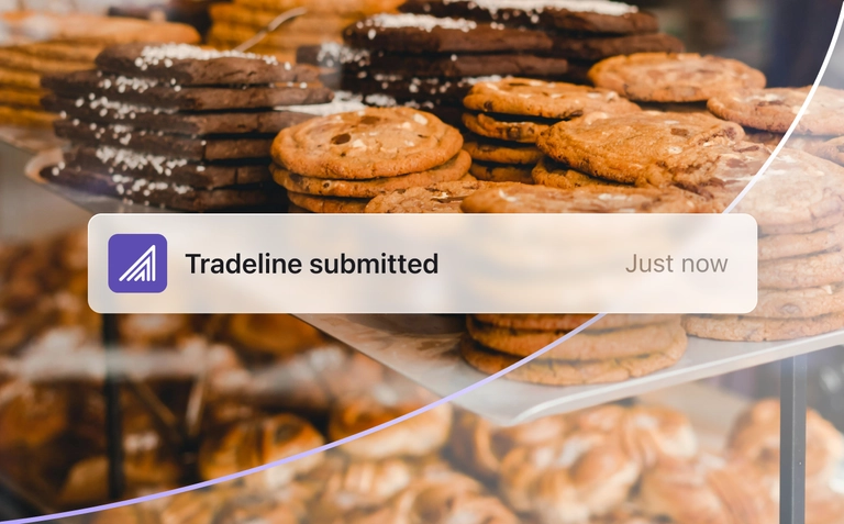Notification banner confirming tradeline submitted over a bakery display background.